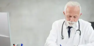 Lekarz w białym fartuchu wypełnia dokumentację przy komputerze w gabinecie