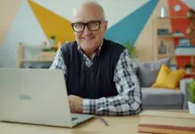 Starszy uśmiechnięty mężczyzna w okularach pracujący przy laptopie