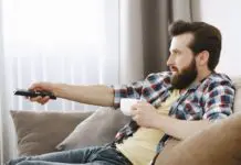 Mężczyzna siedzący na kanapie z pilotem do telewizora w dłoni