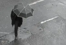 Mężczyzna z parasolem przechodzi przez ulicę w deszczu