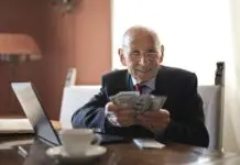 Uśmiechnięty starszy mężczyzna liczy banknoty przy stole