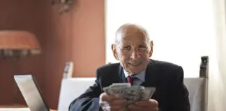 Uśmiechnięty starszy mężczyzna liczy banknoty przy stole