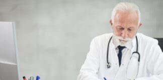 Lekarz w białym fartuchu wypełnia dokumentację przy komputerze w gabinecie