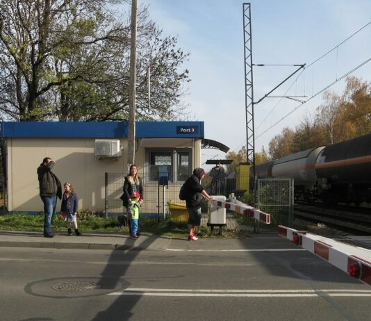 Rogatki zamknęły się, a auto stoi na torach. Ekspert PLK: o życiu decyduje 11 sekund Przejazd kolejowy z opuszczonymi rogatkami, w tle przejeżdżający pociąg towarowy