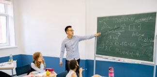 Dziś Dzień Edukacji Narodowej. Skąd się wzięło święto nauczycieli i czy uczniowie mają wolne? Nauczyciel wskazuje na tablicę podczas lekcji w klasie